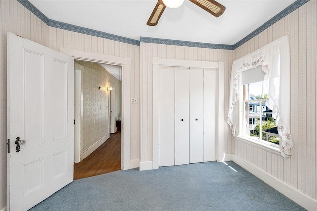 unfurnished bedroom featuring carpet, a ceiling fan, wallpapered walls, baseboards, and a closet