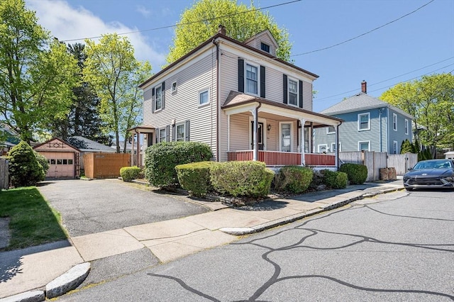 american foursquare style home featuring covered porch, fence, an outbuilding, and a detached garage