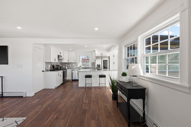 kitchen featuring dark hardwood / wood-style floors, backsplash, a breakfast bar, white cabinets, and appliances with stainless steel finishes