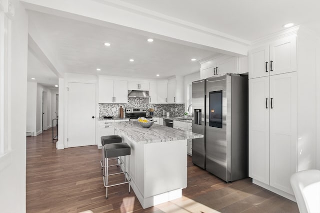 kitchen featuring light stone countertops, stainless steel appliances, dark wood-type flooring, white cabinetry, and a kitchen island