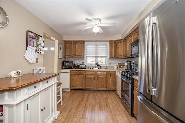 kitchen with sink, ceiling fan, appliances with stainless steel finishes, light hardwood / wood-style floors, and decorative backsplash