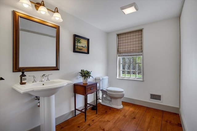 half bathroom featuring visible vents, wood-type flooring, toilet, baseboards, and a sink