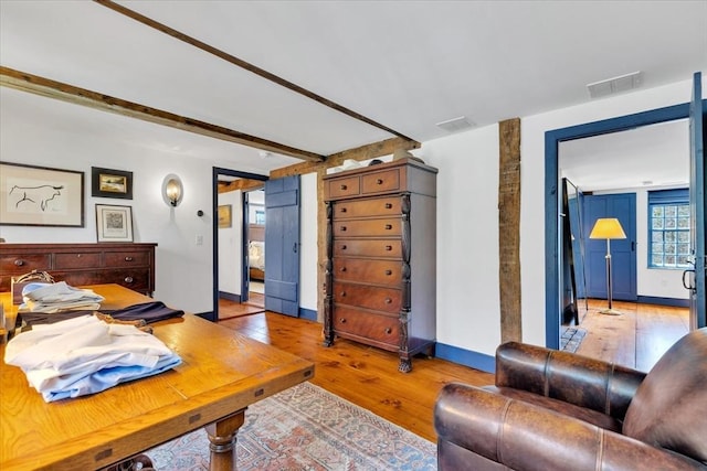 bedroom with baseboards, visible vents, beam ceiling, and light wood-style floors