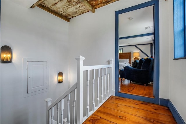 hallway with visible vents, wood finished floors, an upstairs landing, and beamed ceiling