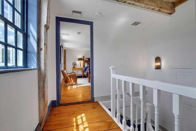 hall with baseboards, an upstairs landing, light wood-type flooring, and visible vents