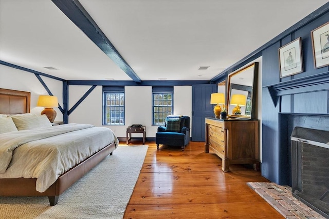 bedroom with beamed ceiling, a fireplace, hardwood / wood-style flooring, and visible vents