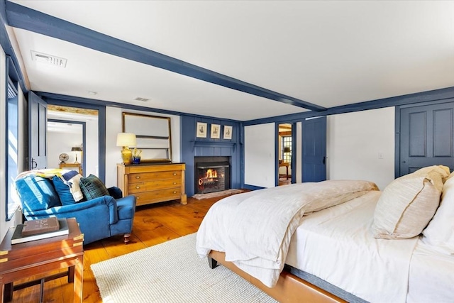 bedroom featuring wood-type flooring, a lit fireplace, and visible vents