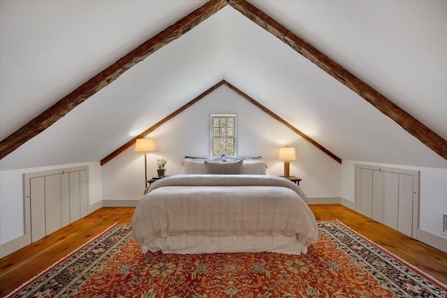 bedroom with lofted ceiling with beams and wood finished floors