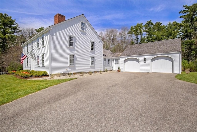 view of home's exterior with an attached garage, aphalt driveway, a yard, and a chimney