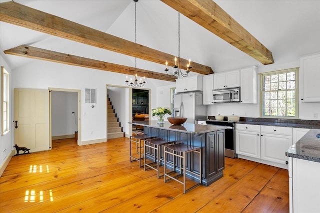 kitchen with vaulted ceiling with beams, appliances with stainless steel finishes, white cabinets, and a kitchen breakfast bar