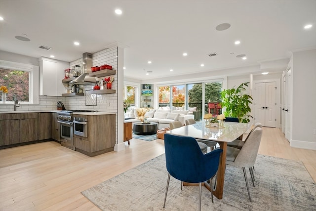 dining space with light wood-type flooring, ornamental molding, and a wealth of natural light