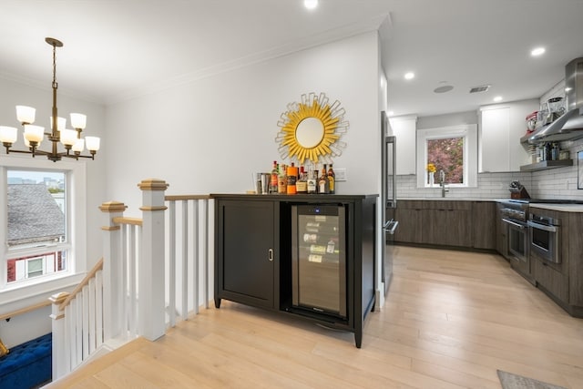 kitchen with dark brown cabinets, light wood-type flooring, wine cooler, a chandelier, and stainless steel oven