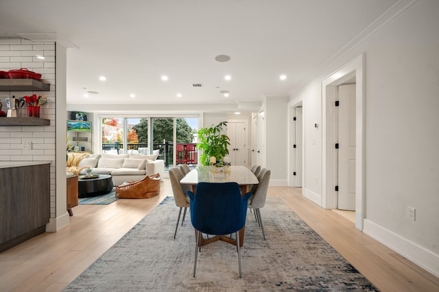 dining room featuring light wood-type flooring, crown molding, and a brick fireplace