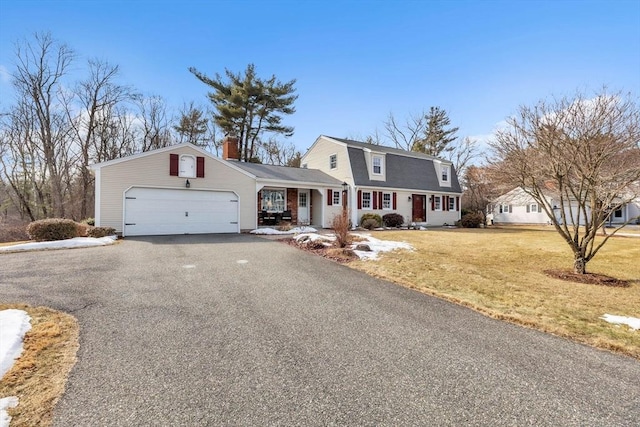 colonial inspired home featuring a chimney, an attached garage, a gambrel roof, a front yard, and driveway