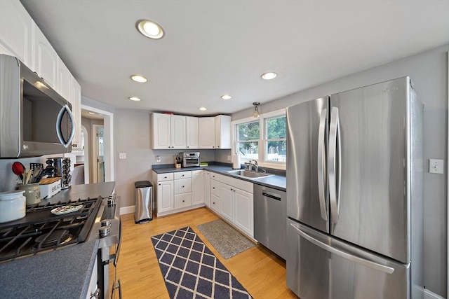 kitchen featuring appliances with stainless steel finishes, a sink, light wood-style flooring, white cabinetry, and recessed lighting