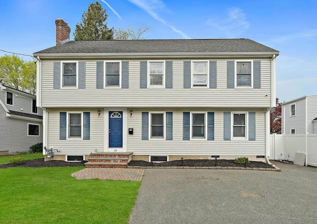 colonial-style house featuring fence, a chimney, and a front lawn