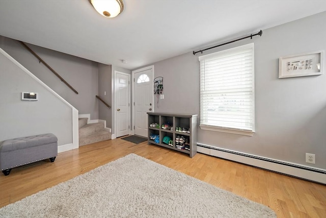 foyer entrance with stairway, baseboard heating, and wood finished floors