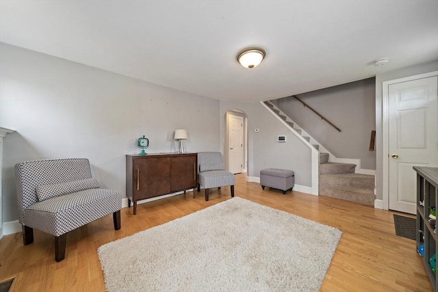 sitting room with arched walkways, stairs, baseboards, light wood-type flooring, and visible vents