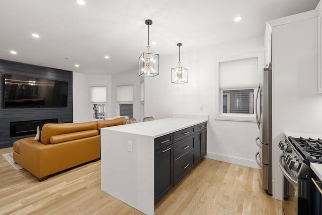 kitchen with decorative light fixtures, a fireplace, light wood-type flooring, appliances with stainless steel finishes, and white cabinets