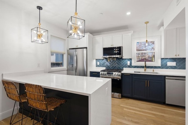 kitchen featuring white cabinetry, a breakfast bar area, appliances with stainless steel finishes, decorative light fixtures, and sink