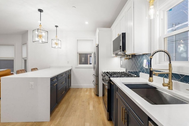 kitchen featuring pendant lighting, white cabinets, range with gas cooktop, sink, and stainless steel fridge