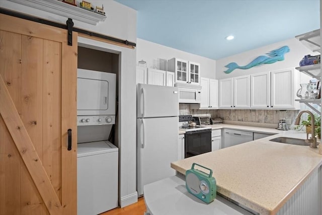 kitchen featuring white appliances, a barn door, backsplash, stacked washer / drying machine, and a sink