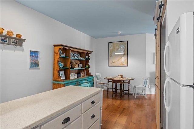 kitchen featuring a barn door, white cabinets, wood finished floors, and freestanding refrigerator