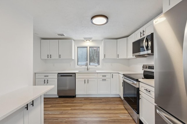 kitchen with appliances with stainless steel finishes, white cabinetry, light hardwood / wood-style floors, and sink