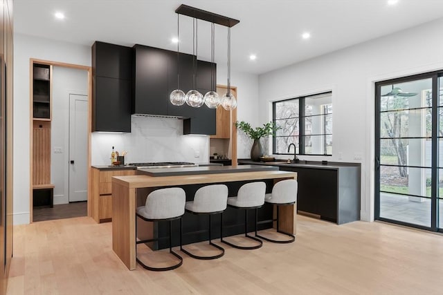 kitchen featuring a center island, light hardwood / wood-style floors, hanging light fixtures, wall chimney range hood, and backsplash