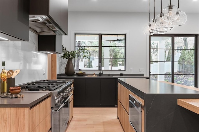 kitchen featuring decorative light fixtures, sink, wall chimney range hood, a kitchen island, and high end range