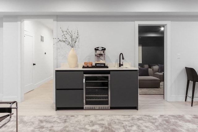 bar featuring sink, beverage cooler, and light hardwood / wood-style flooring