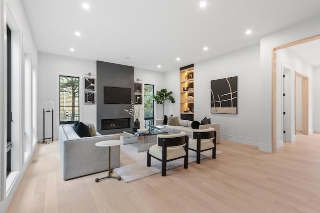 living room featuring a large fireplace, built in shelves, and light hardwood / wood-style floors