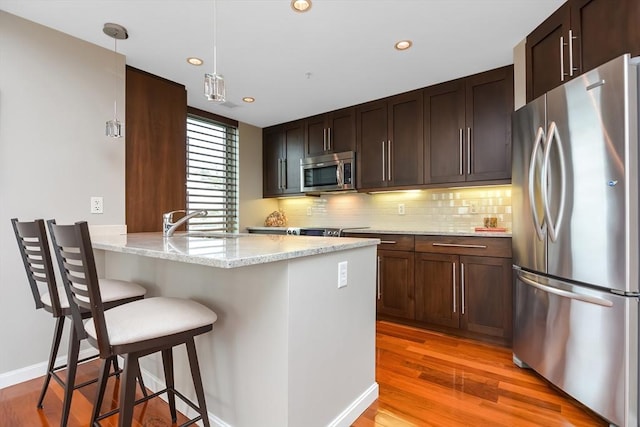 kitchen with appliances with stainless steel finishes, light stone countertops, a kitchen bar, decorative light fixtures, and kitchen peninsula