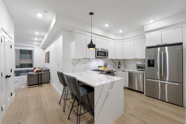 101 Condor St Unit 301A, Boston, MA 02128 - kitchen with appliances with stainless steel finishes, a peninsula, light wood-style floors, white cabinets, and a kitchen bar