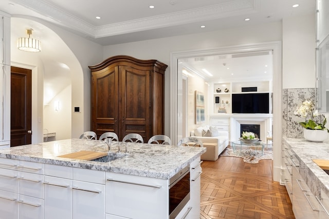 kitchen featuring light stone counters, white cabinetry, a kitchen island, light parquet flooring, and built in features