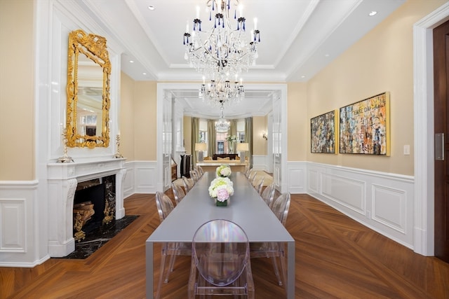 dining space with a high end fireplace, parquet flooring, a chandelier, a raised ceiling, and ornamental molding