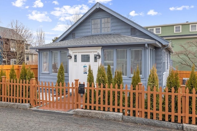 bungalow featuring a fenced front yard and roof with shingles