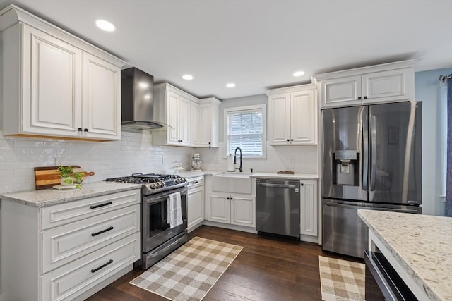 kitchen featuring dark wood-type flooring, appliances with stainless steel finishes, white cabinetry, wall chimney exhaust hood, and a sink