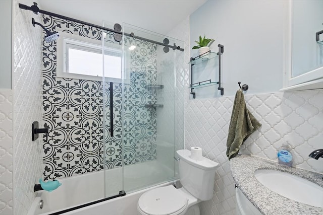 bathroom featuring vanity, a wainscoted wall, bath / shower combo with glass door, tile walls, and toilet