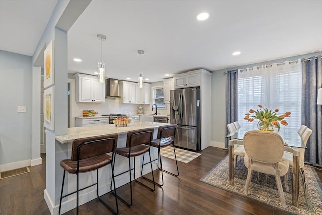 kitchen with dark wood-style floors, white cabinetry, stainless steel appliances, and wall chimney range hood