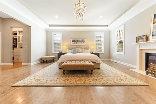 bedroom featuring a tray ceiling, a fireplace with flush hearth, baseboards, and hardwood / wood-style flooring