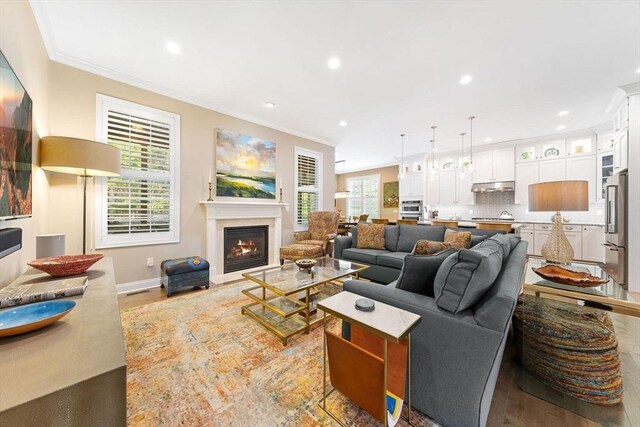 living area featuring crown molding, recessed lighting, a warm lit fireplace, and light wood-type flooring