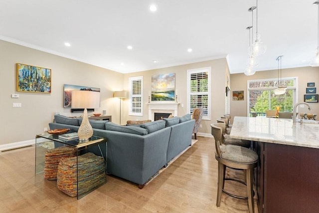 living room with crown molding, baseboards, light wood finished floors, a warm lit fireplace, and recessed lighting
