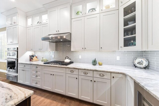 kitchen with appliances with stainless steel finishes, white cabinets, a warming drawer, under cabinet range hood, and dark wood-type flooring