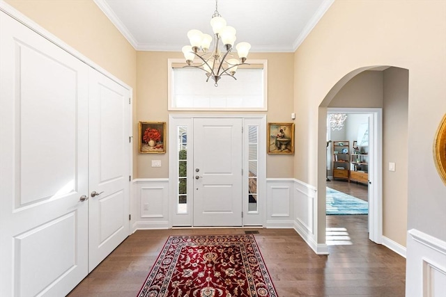 entryway with an inviting chandelier, arched walkways, a wainscoted wall, and dark wood-style floors