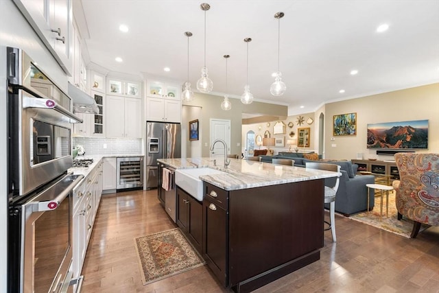 kitchen with crown molding, wine cooler, open floor plan, a sink, and appliances with stainless steel finishes
