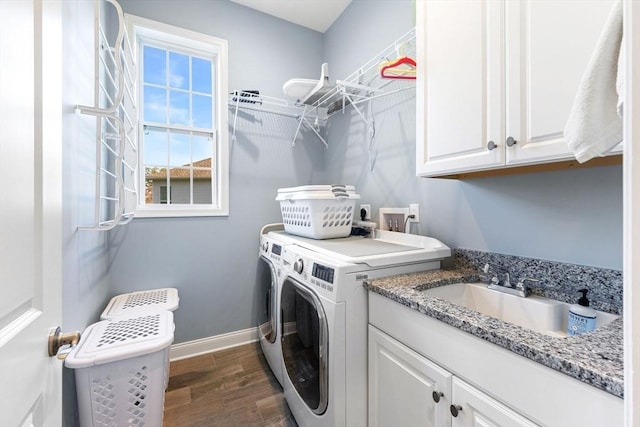 clothes washing area featuring washing machine and clothes dryer, dark wood finished floors, cabinet space, a sink, and baseboards