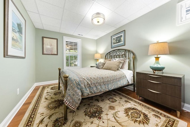 bedroom with baseboards, a paneled ceiling, and wood finished floors