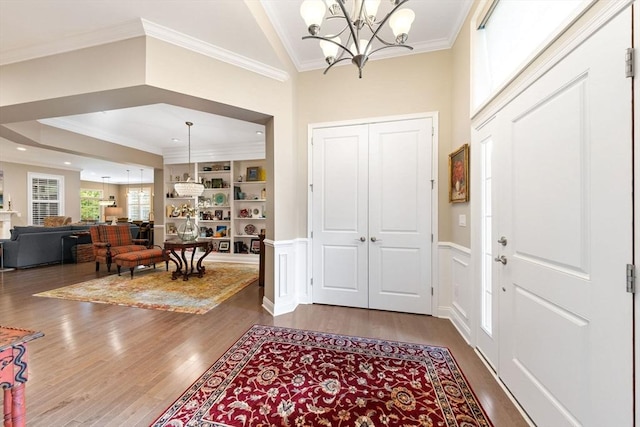 foyer featuring a towering ceiling, wainscoting, wood finished floors, a chandelier, and ornamental molding