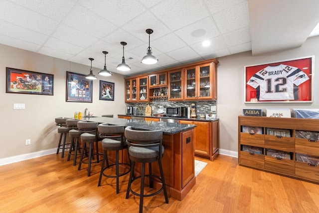 bar featuring decorative backsplash, indoor wet bar, baseboards, a drop ceiling, and light wood-style flooring
